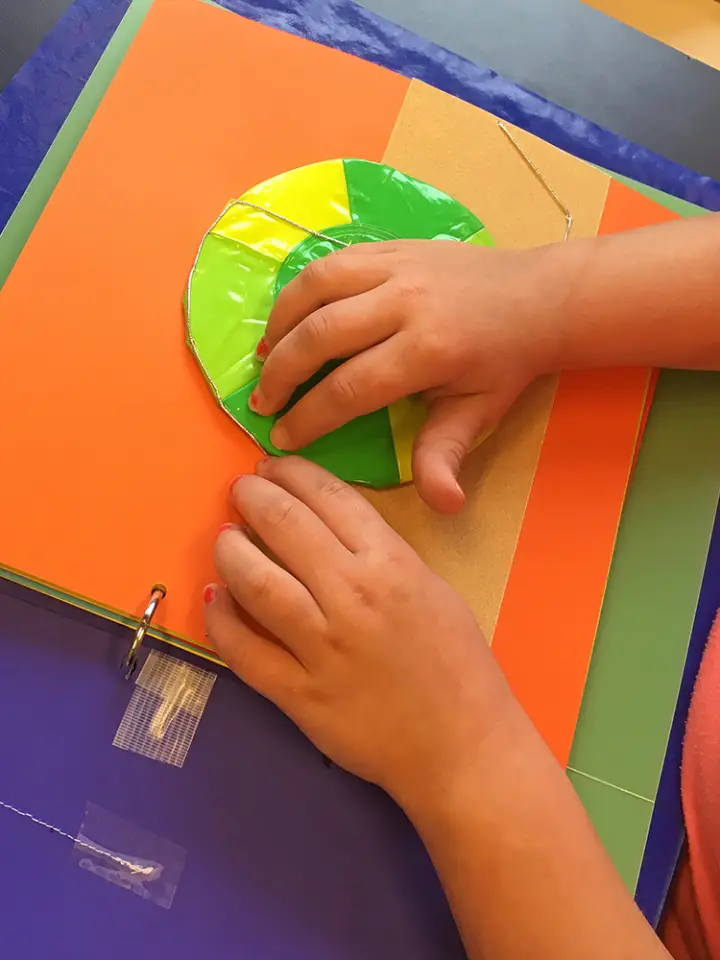 A child follows the thread on an illustration page using both hands.